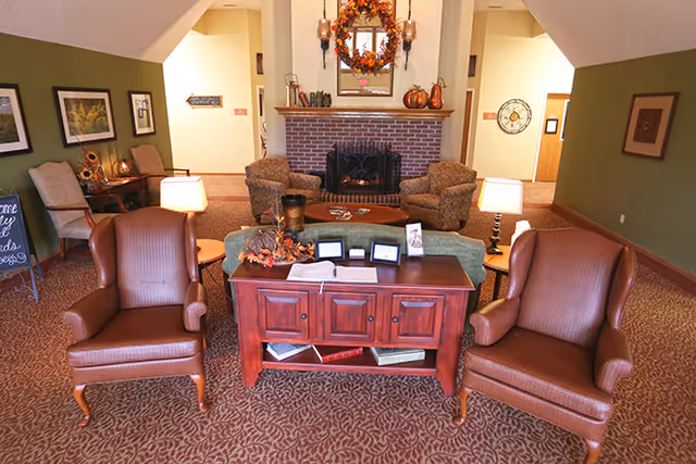 Cozy senior living lounge with leather chairs, brick fireplace, and a wooden front desk.