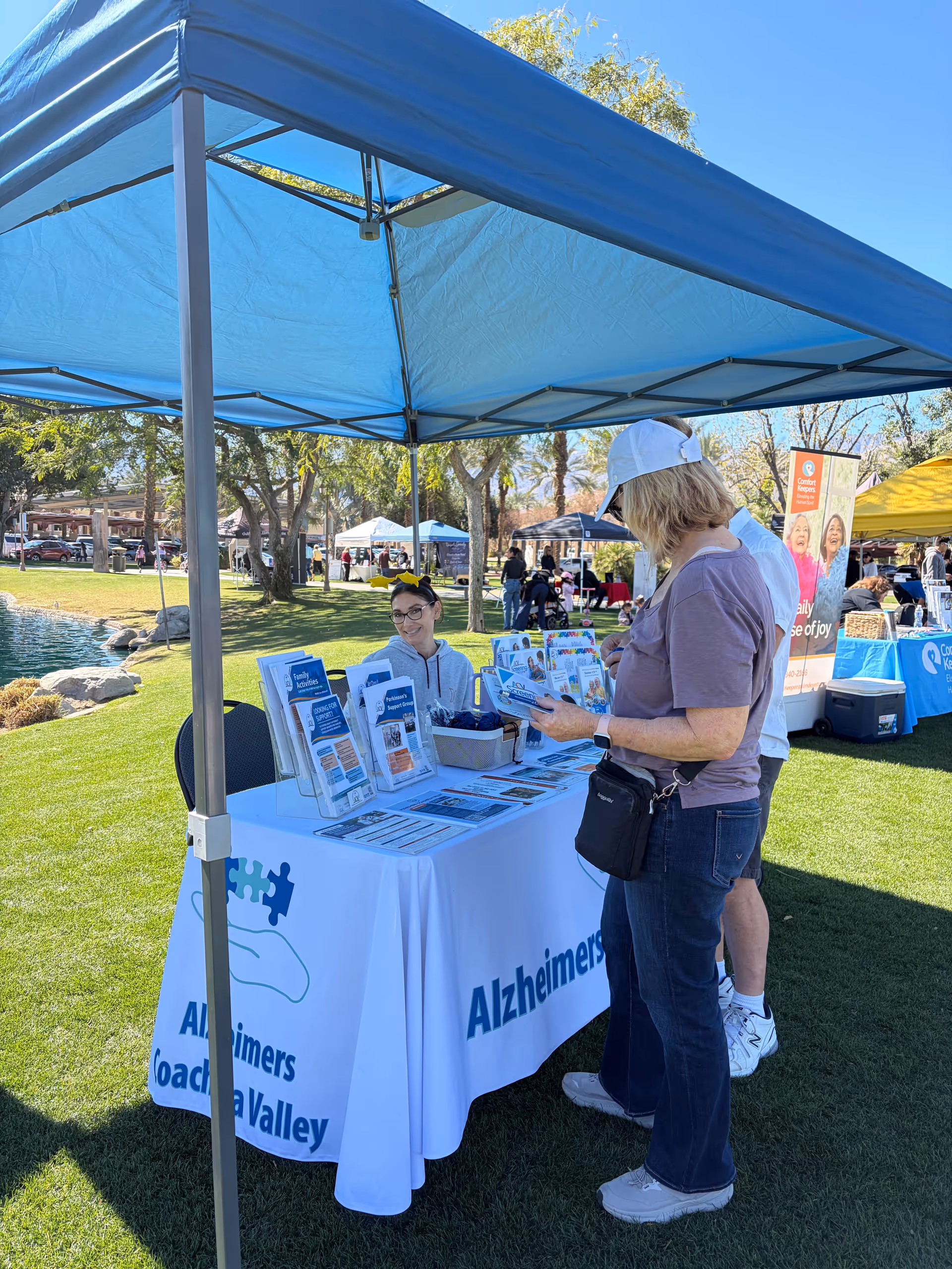 Outdoor event under a blue canopy with an Alzheimer's information table and attendees.