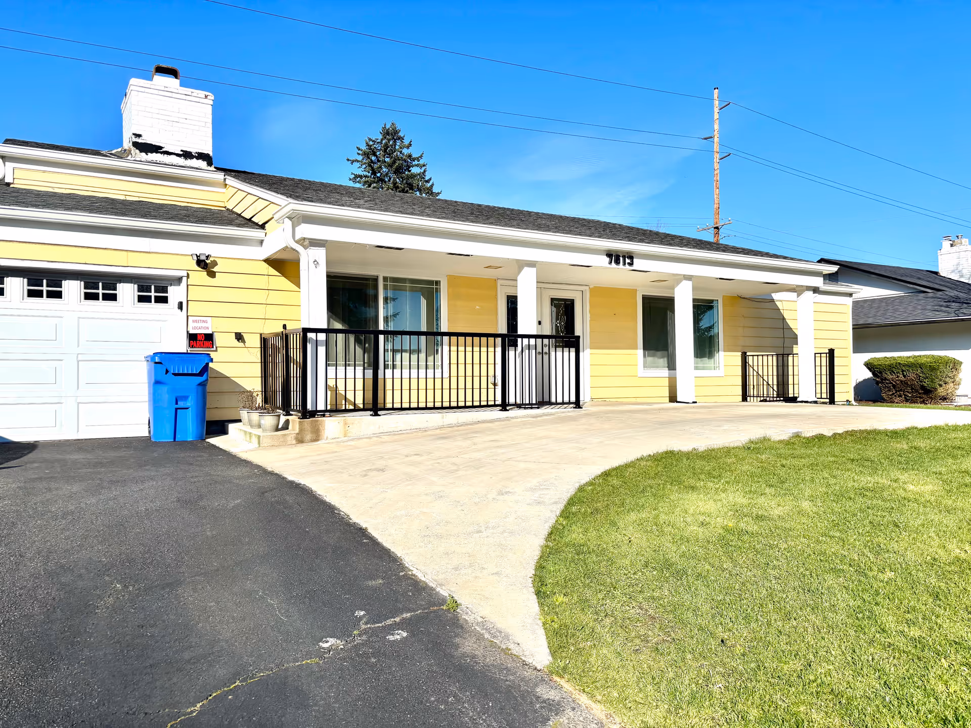 Yellow single-story building exterior with white columns, black railing, and a curved driveway.