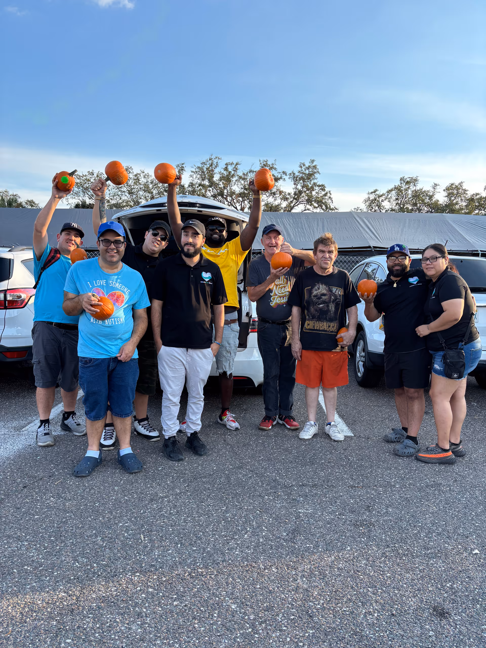 A diverse group of people outdoors, holding pumpkins in a parking lot.