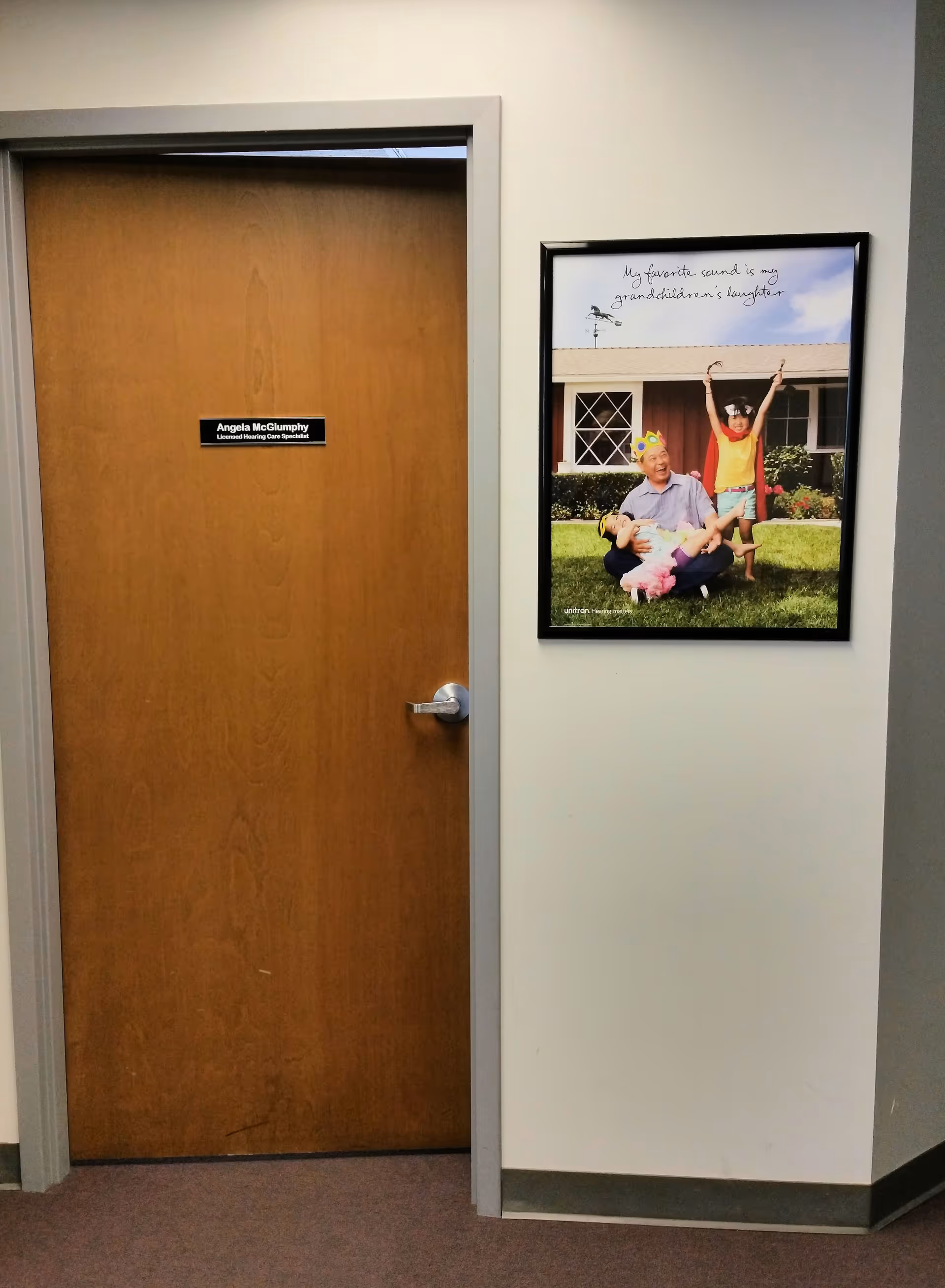 Wooden interior door with a nameplate beside a framed outdoor photo in a hallway.