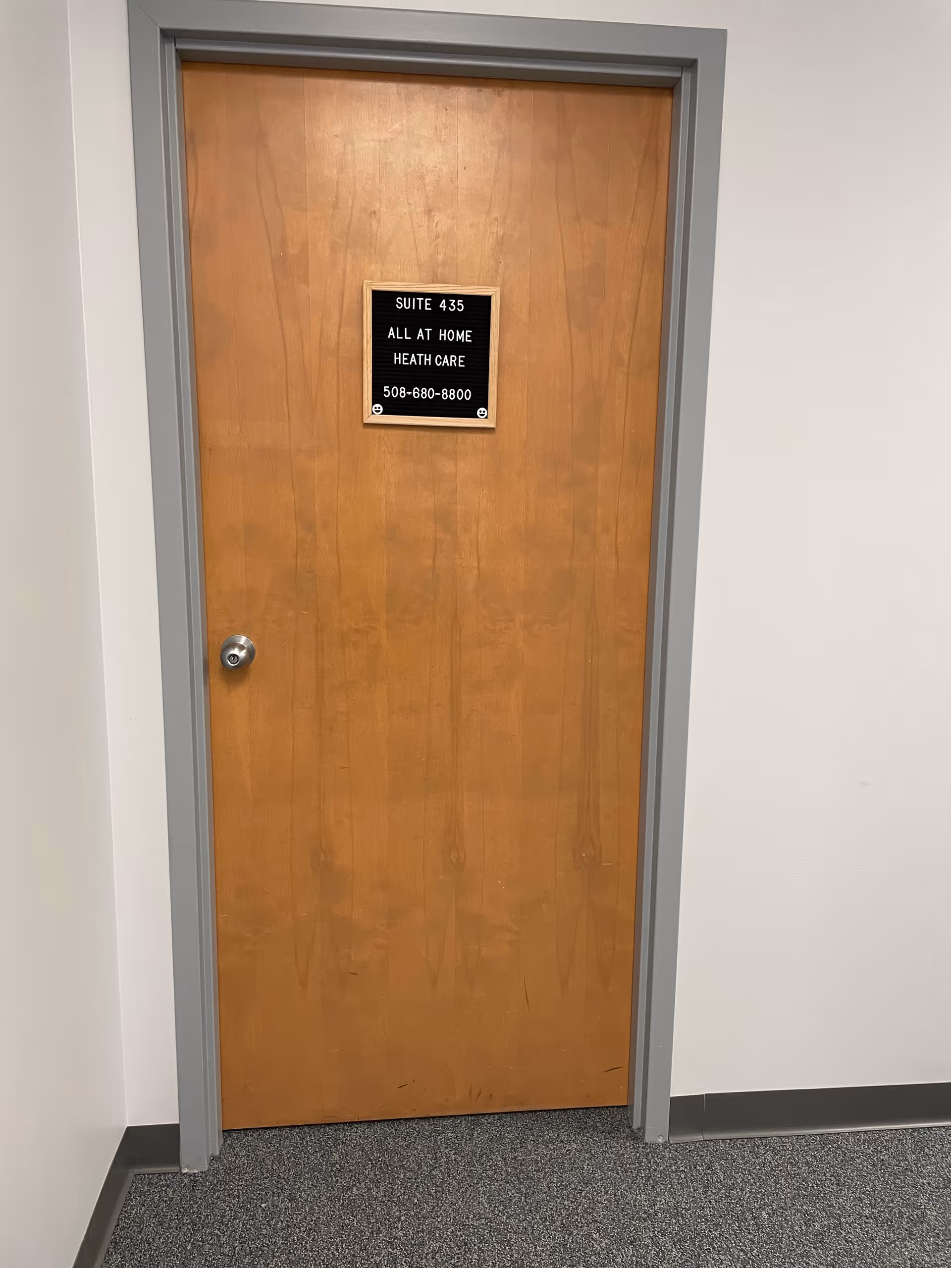 Wooden interior door with a sign for Suite 435 All At Home Health Care in hallway.