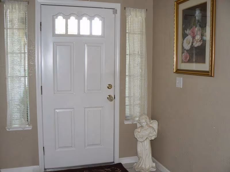 Indoor entryway with a white front door, two side windows, a framed painting, and a statue.