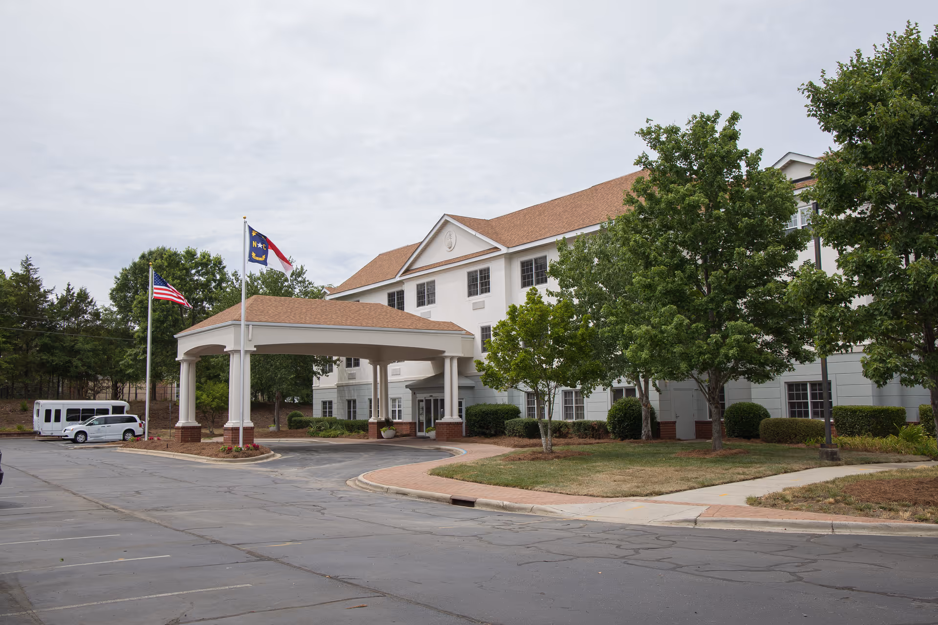 Front view of The Charlotte senior living facility with porte-cochère and flags