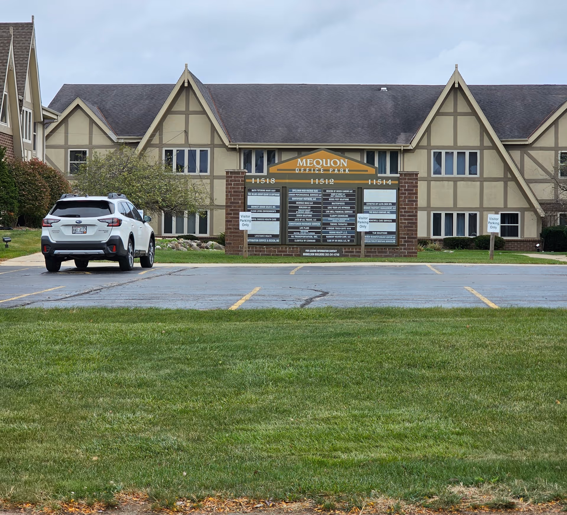 Exterior view of a Tudor-style office park building with a large sign and parking lot.