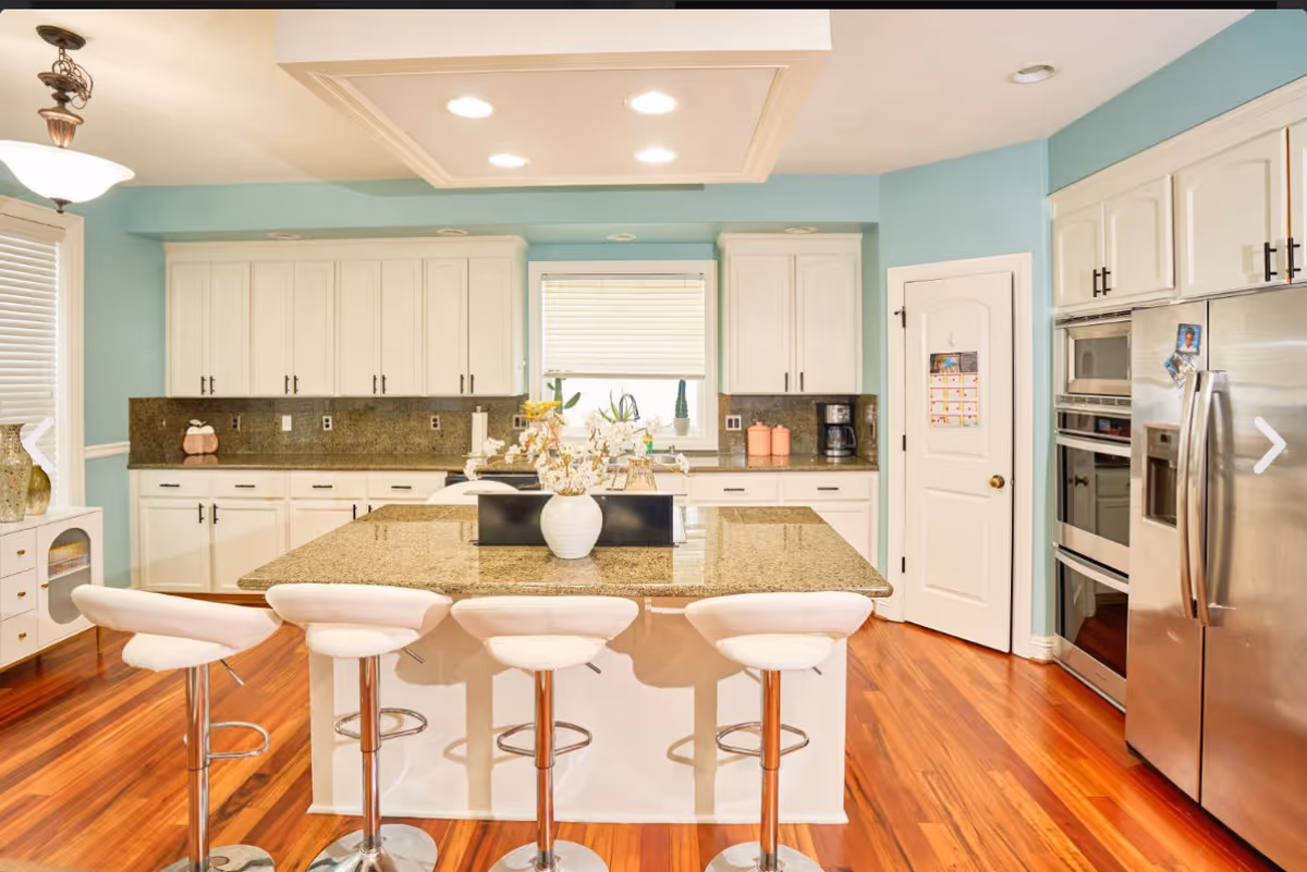 Modern kitchen with island, white cabinets, stainless appliances, and teal walls.