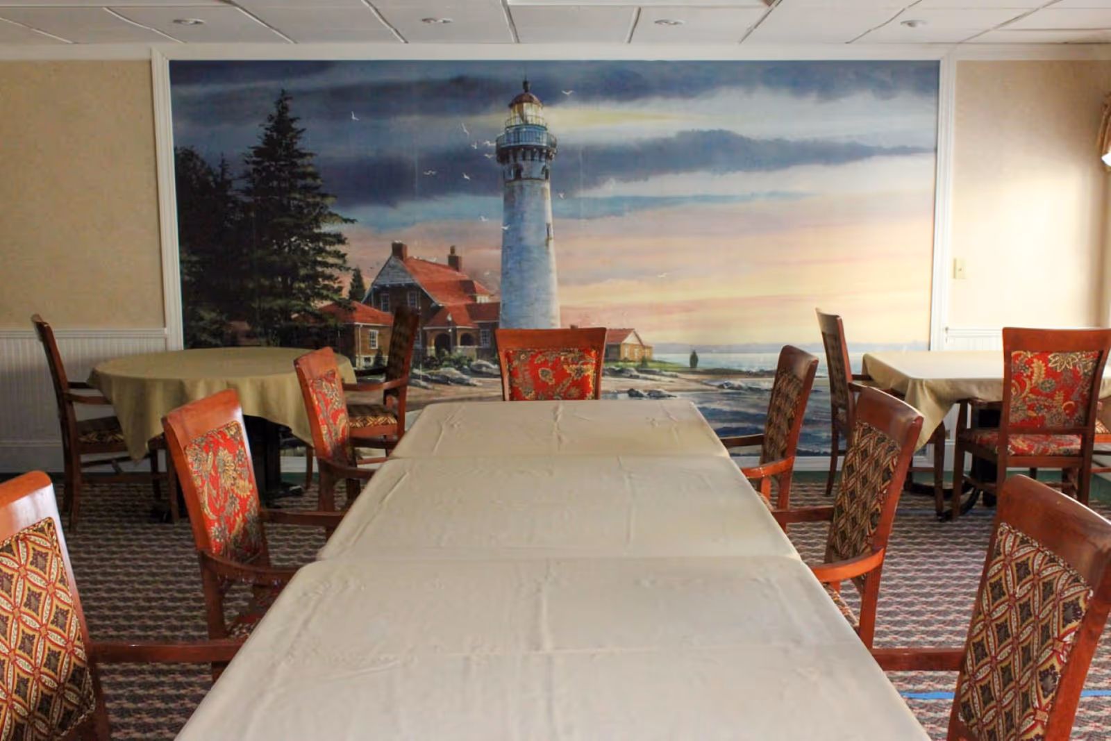 An indoor dining room with tables, chairs, and a lighthouse mural.