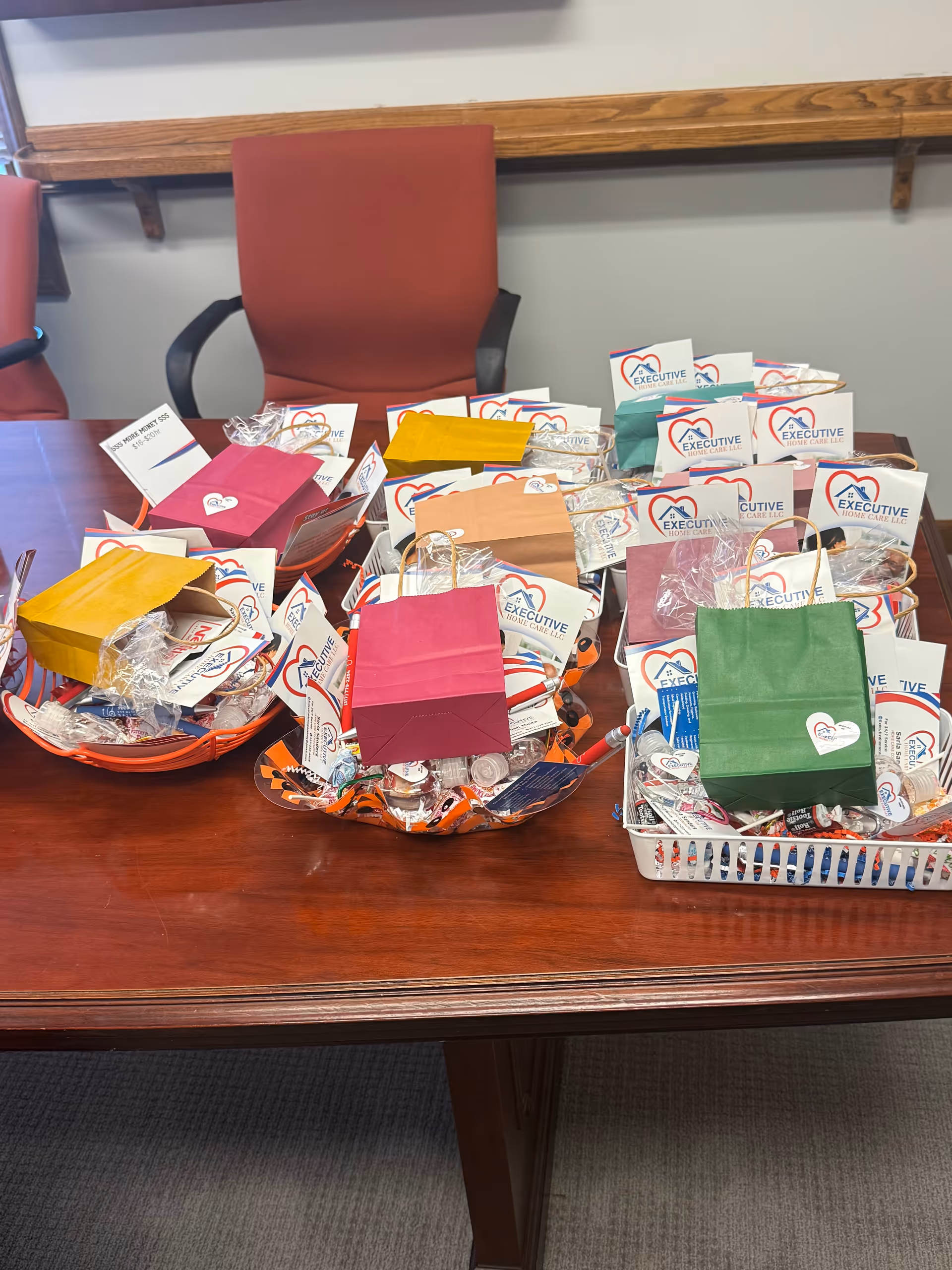 Several gift baskets with colorful envelopes and Executive Care LLC branding on a wooden conference table.