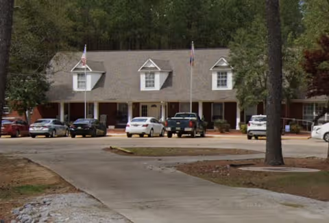 Front view of Oak Tree Manor Assisted Living building with parked cars and trees.