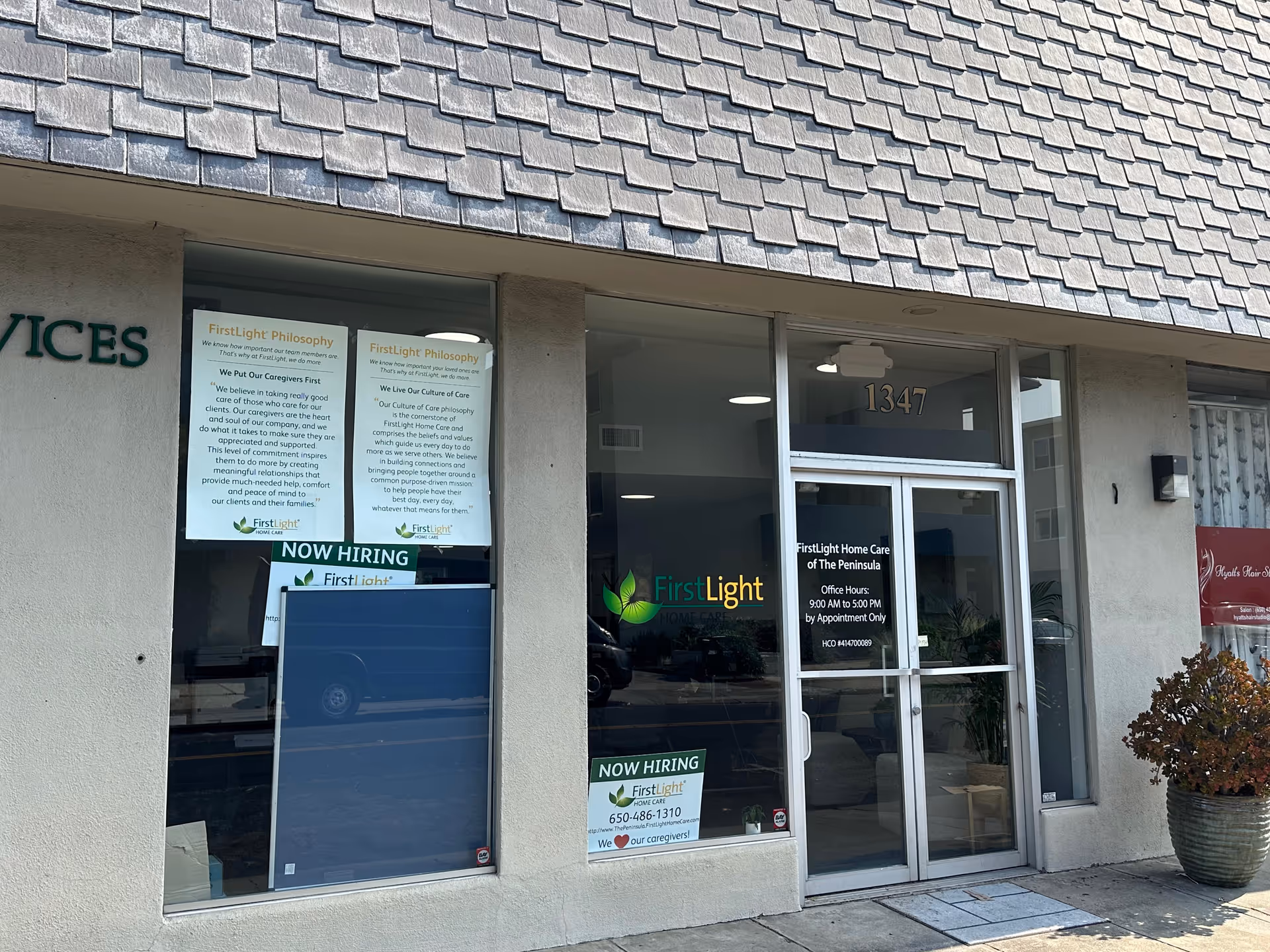Front view of a FirstLight Home Care storefront with glass doors, windows, and hiring signs.