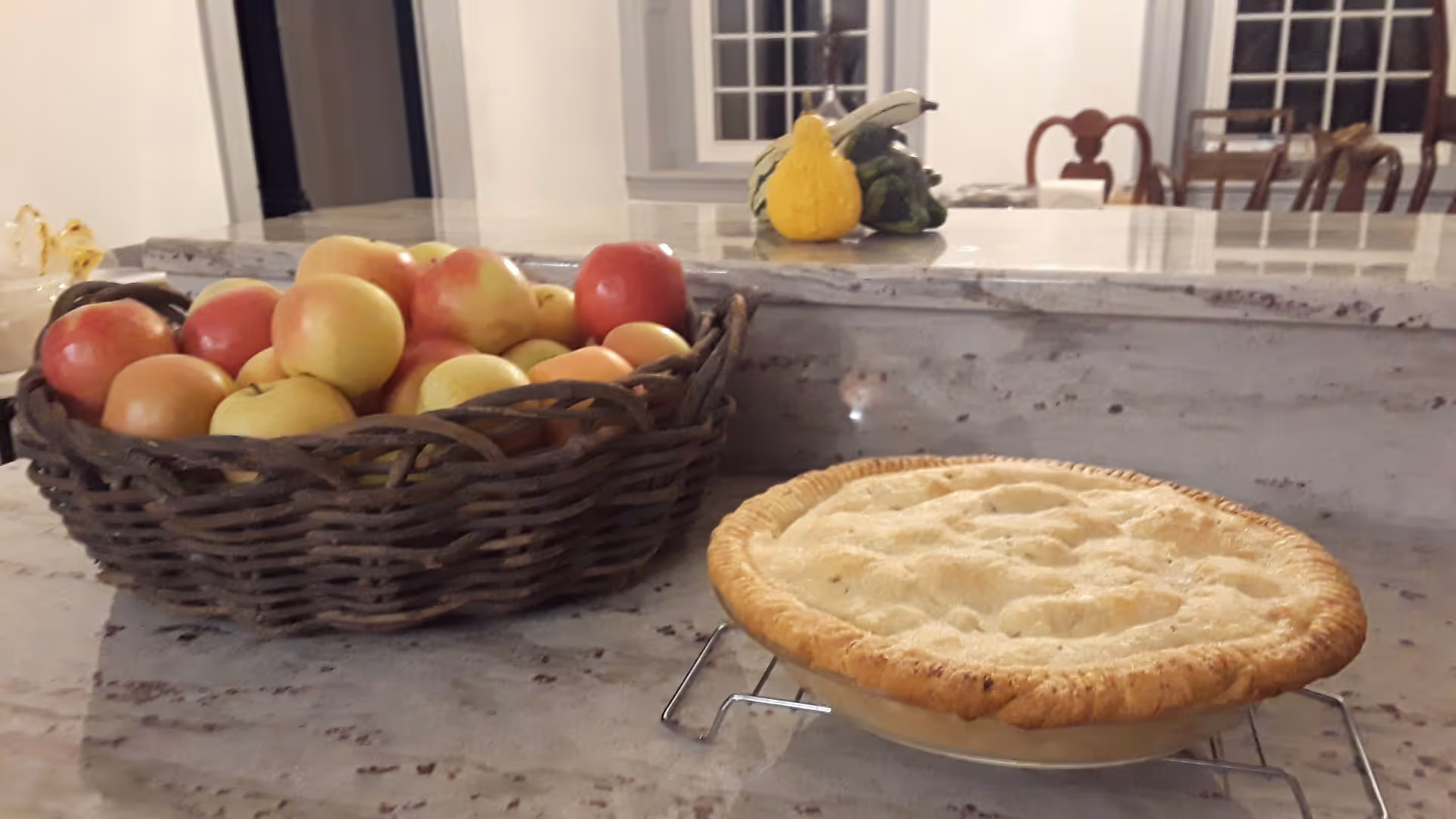 Basket of apples and a pie on a kitchen counter in a cozy dining area.