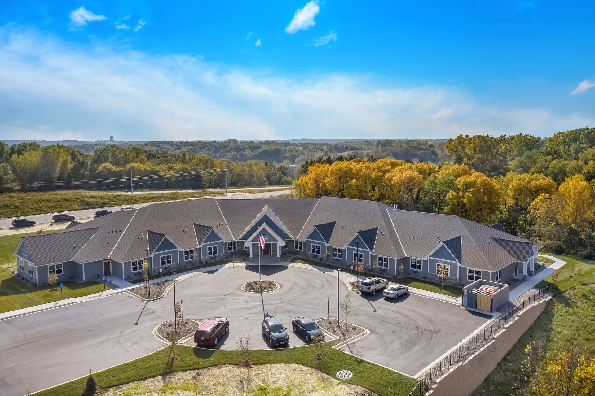 A single-story senior living facility with a circular driveway, flagpole, and parking.