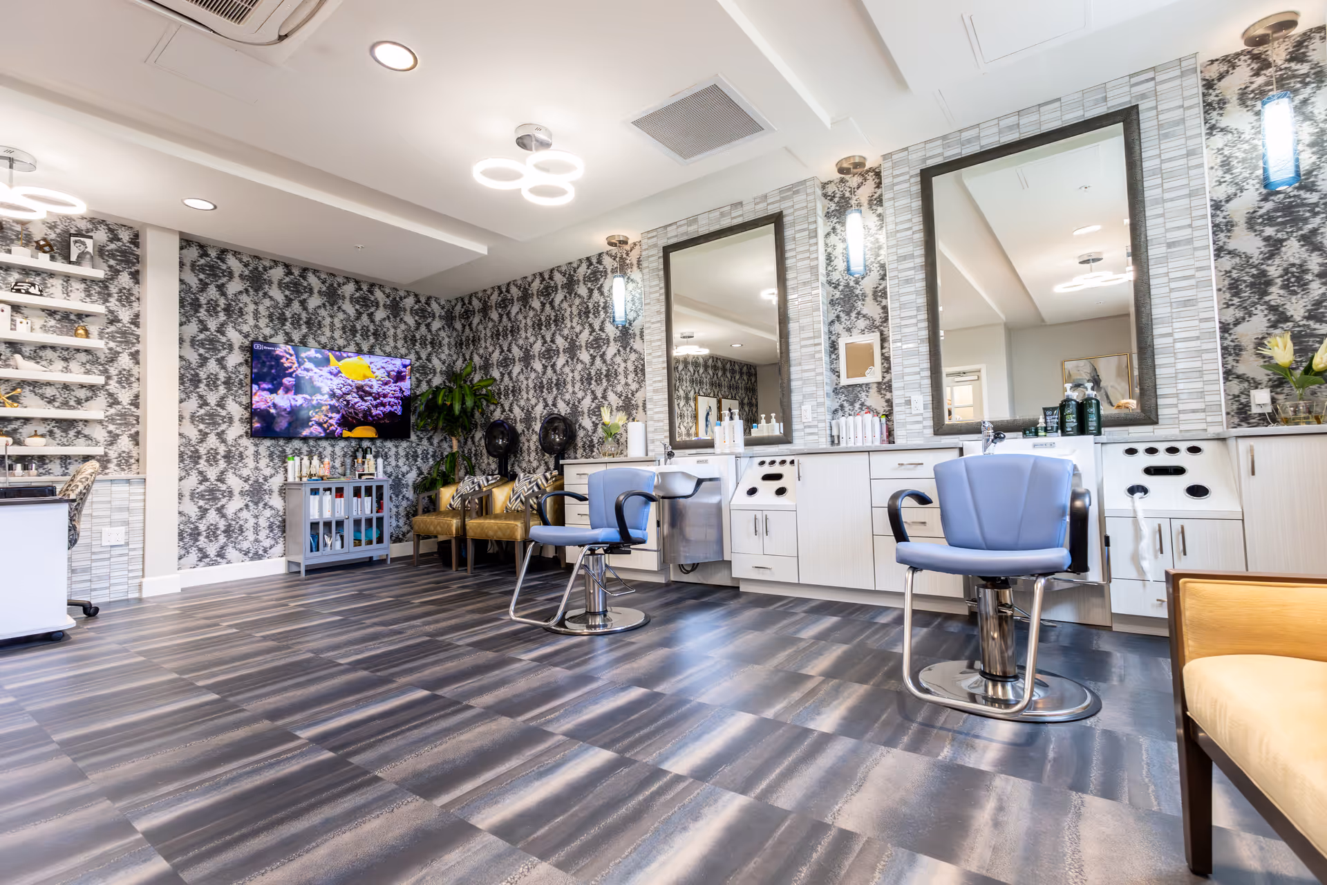 Modern senior living salon with blue chairs, mirrors, and patterned wallpaper.