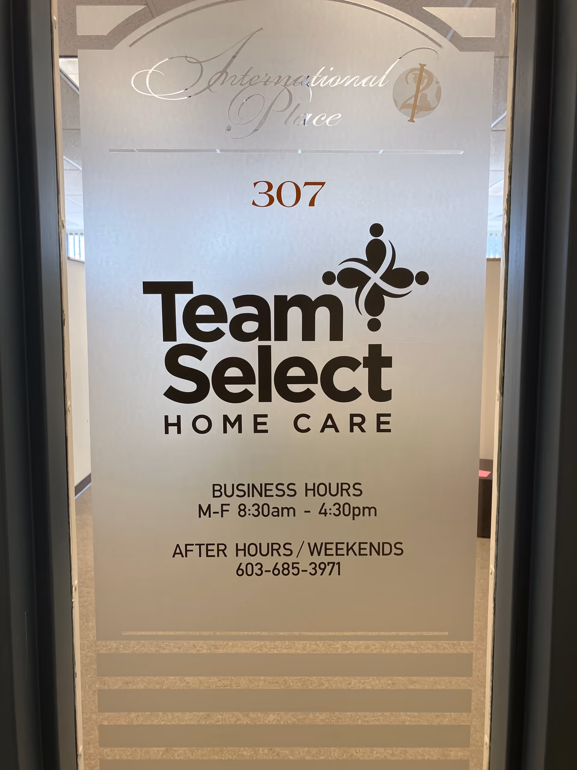 Glass door sign displaying Team Select Home Care branding and hours in an interior hallway.