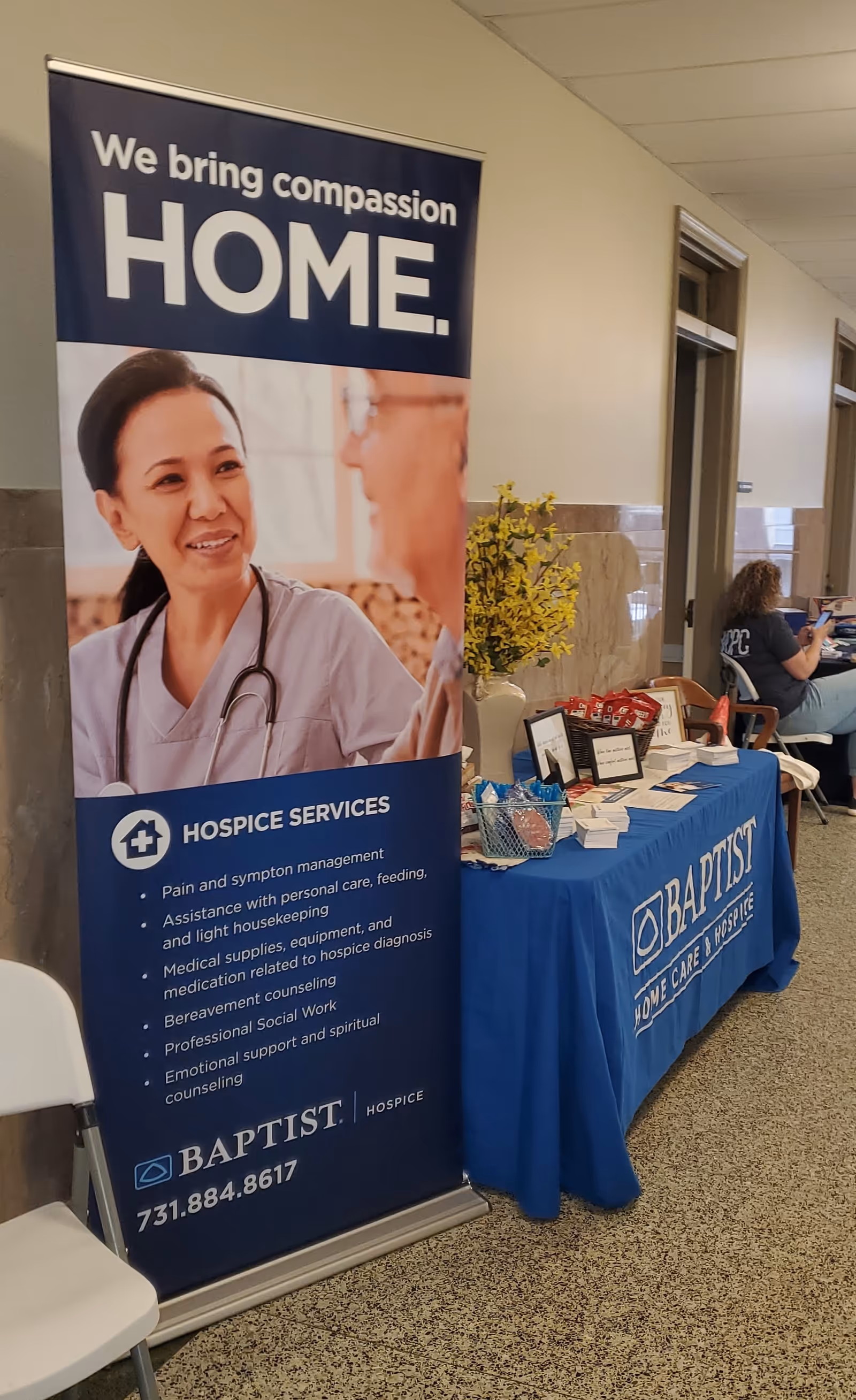 Indoor hallway with a large hospice banner and blue display table.