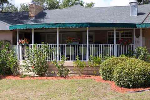 Front porch of Sunshine Assisted Living with railing, green awning, and flowering plants.