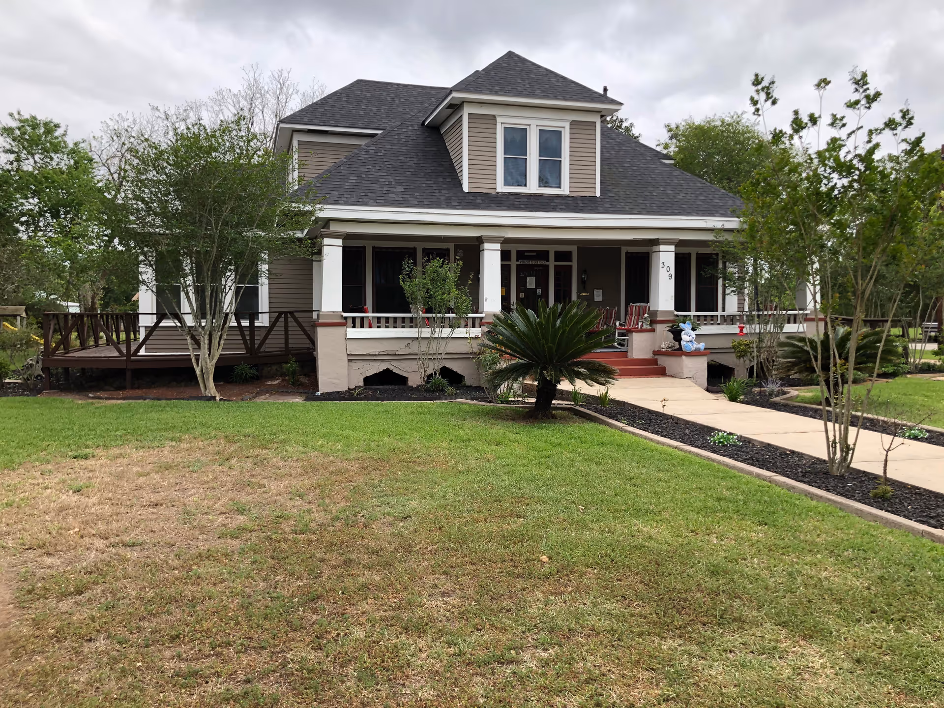 A two-story senior living facility exterior with a wide front porch and manicured landscaping.