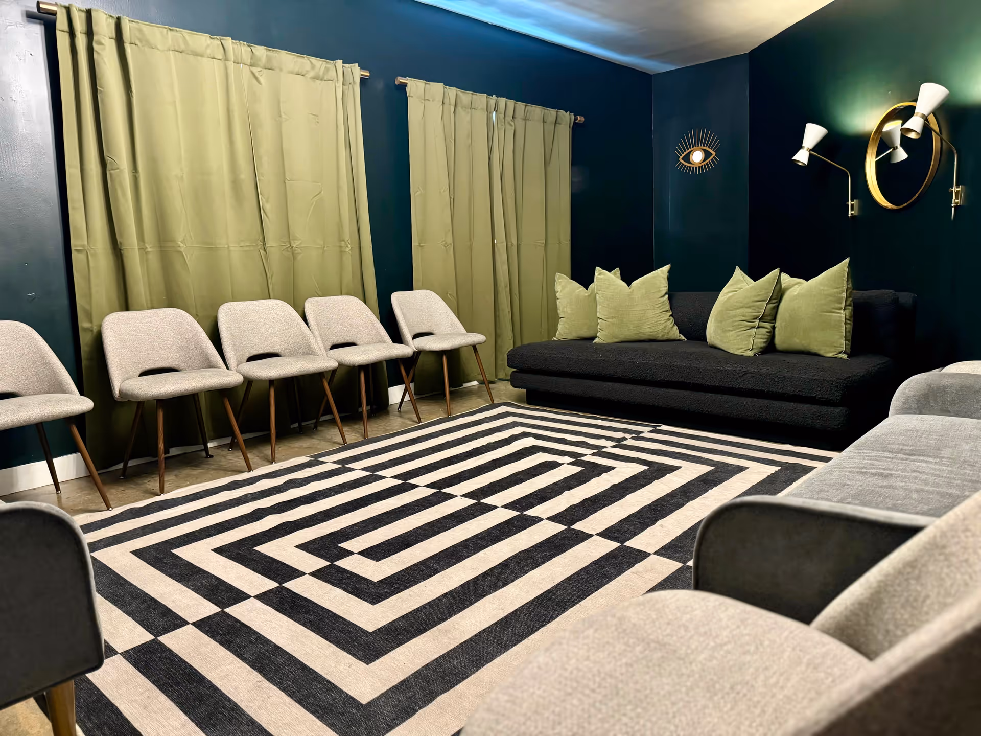 Contemporary lounge with beige chairs, dark sofa, green pillows, curtains, and geometric rug.