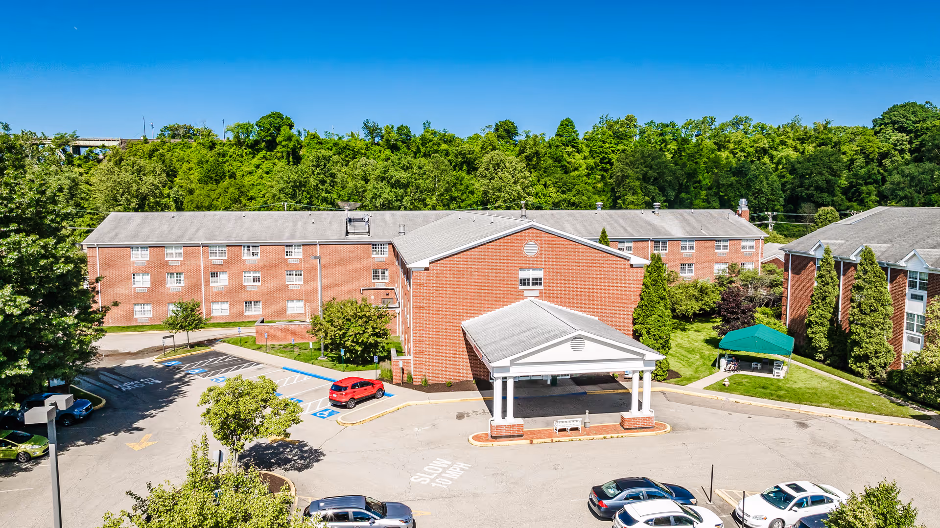 Aerial view of The Villages of Harmar brick senior living facility with covered entrance and parking.