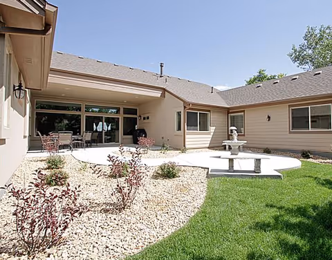 Outdoor courtyard of a senior living facility with patio furniture, gravel beds, and a fountain.