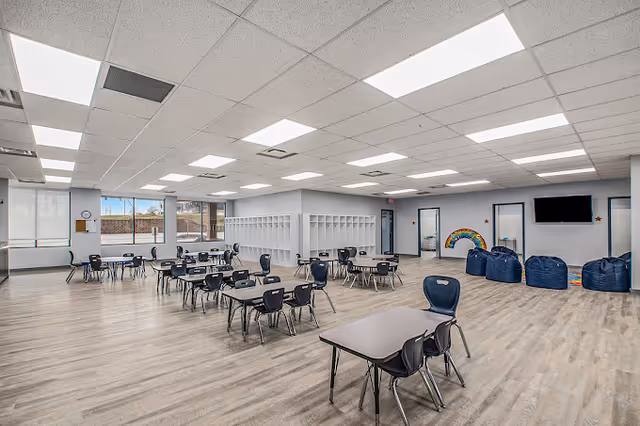 Bright interior multipurpose room with tables, chairs, lockers, windows, and a bean-bag area.