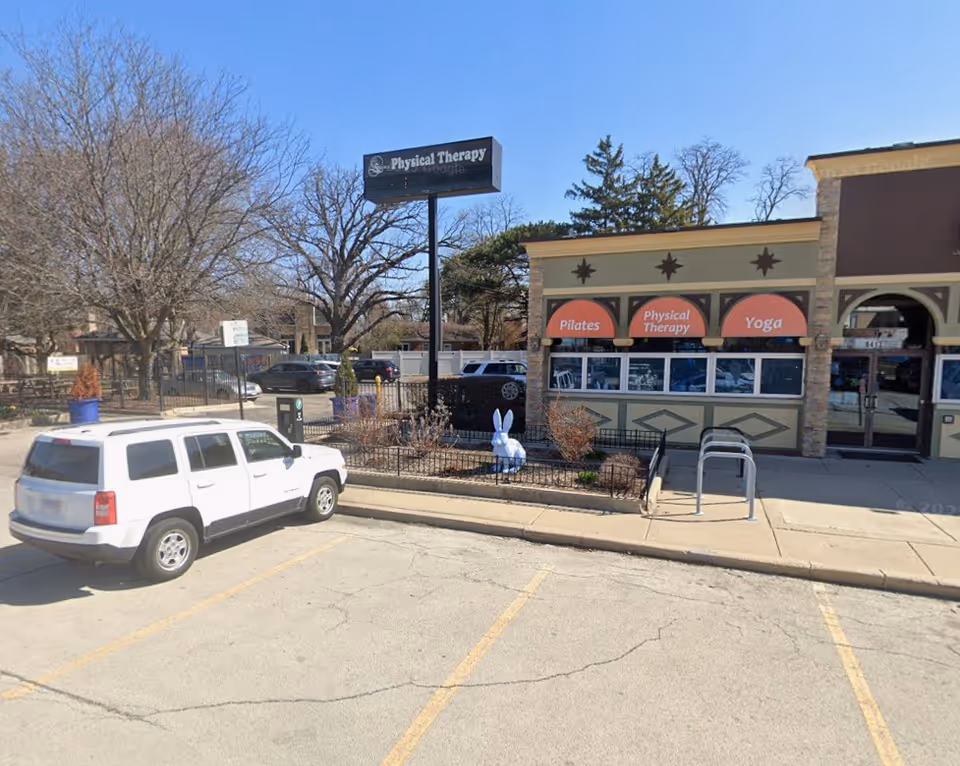 Exterior view of a strip storefront with Pilates and Physical Therapy signage and a parked SUV.
