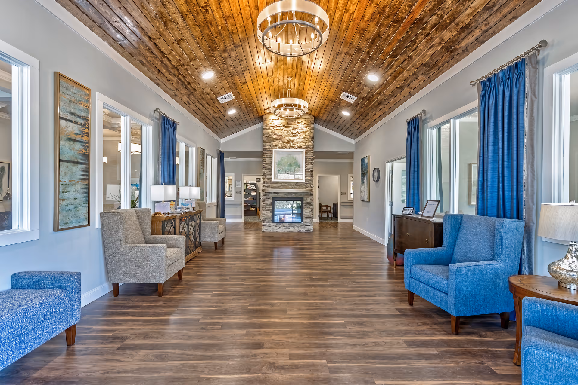 Bright senior living lobby with wood ceiling, stone fireplace, and blue seating along walls.