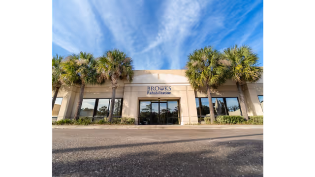 Beige Brooks Rehabilitation front entrance flanked by palm trees under a blue sky.