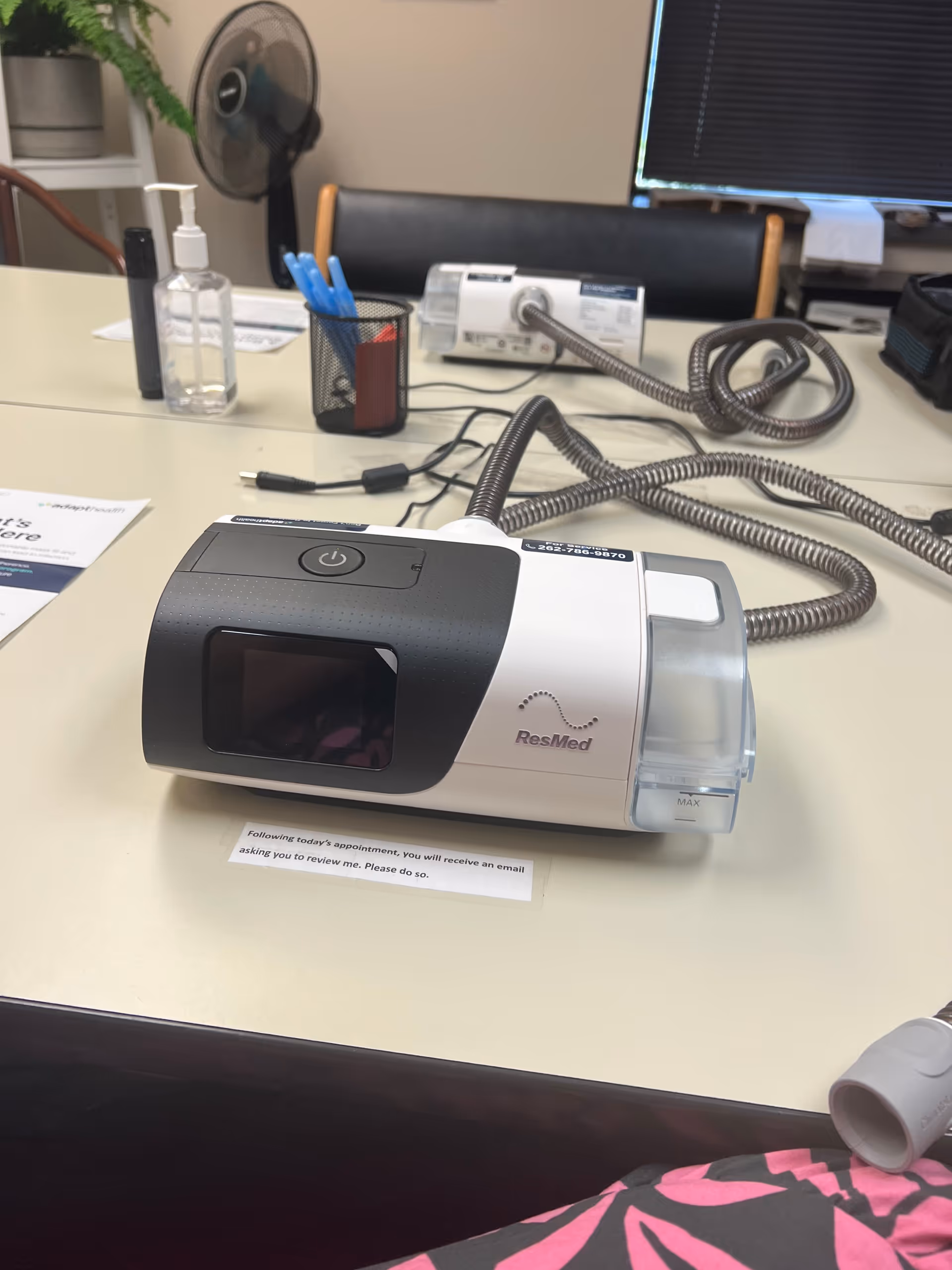 CPAP machine on a desk in a clinic, with tubing and sanitizer nearby.