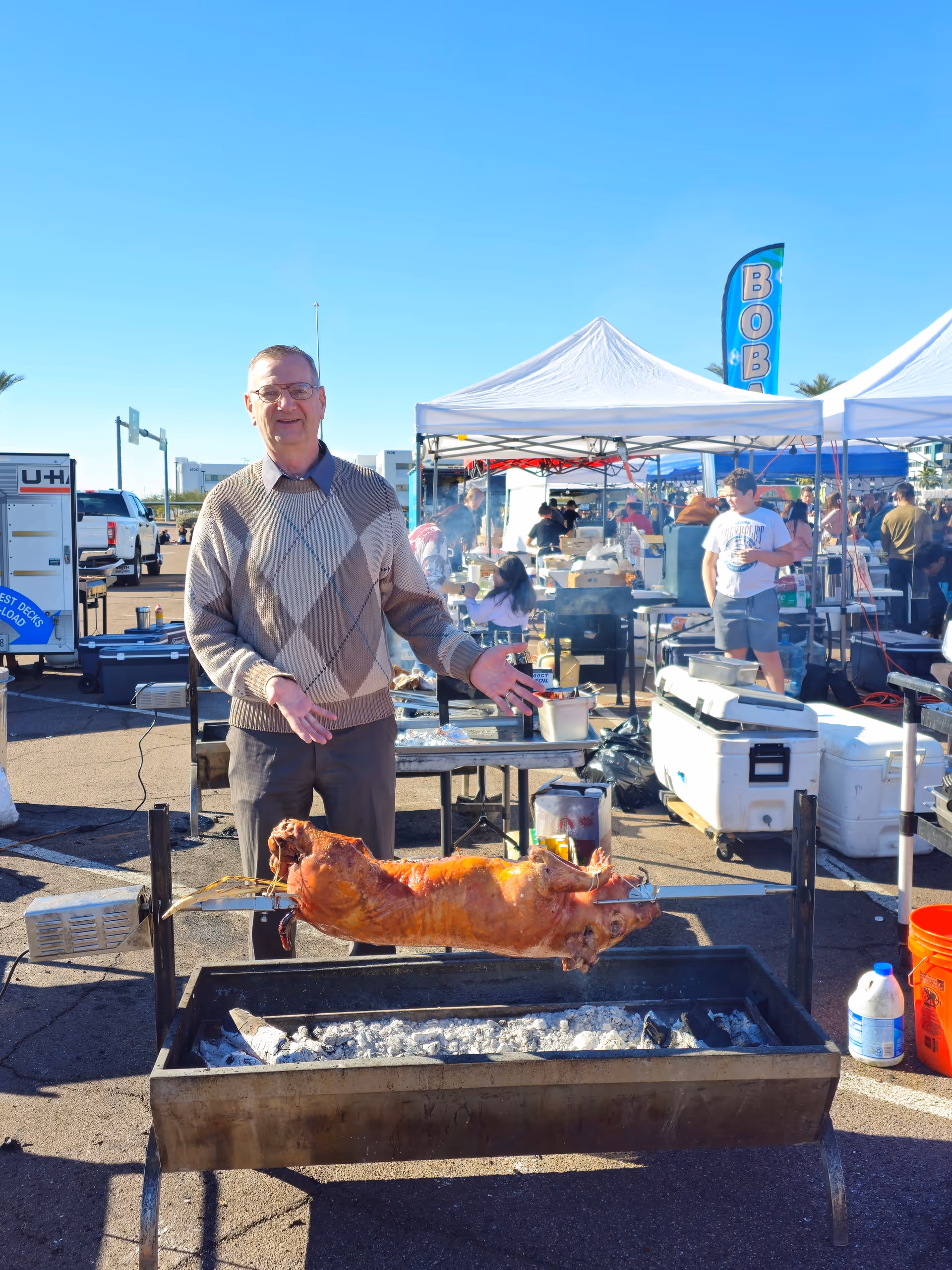 Man stands at an outdoor barbecue grill with a roasted pig on a spit.