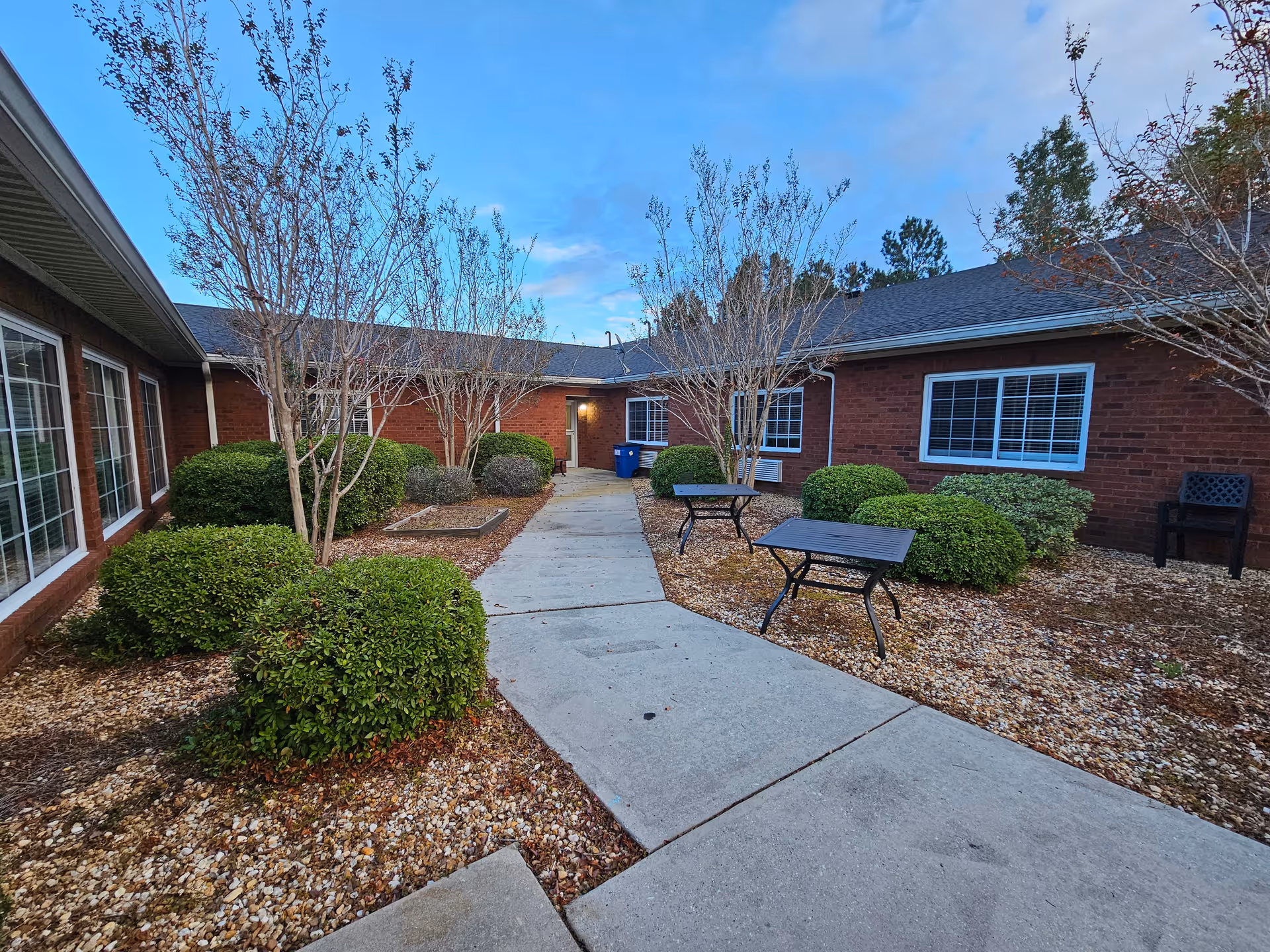 Outdoor courtyard of Leland House with a curved walkway, leafless trees, and metal tables.
