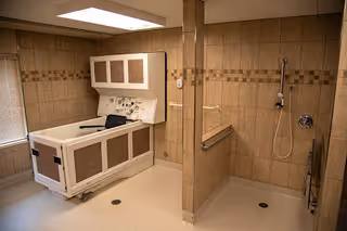 Accessible bathing room with a walk-in bathtub and an open tiled shower area with grab bars.