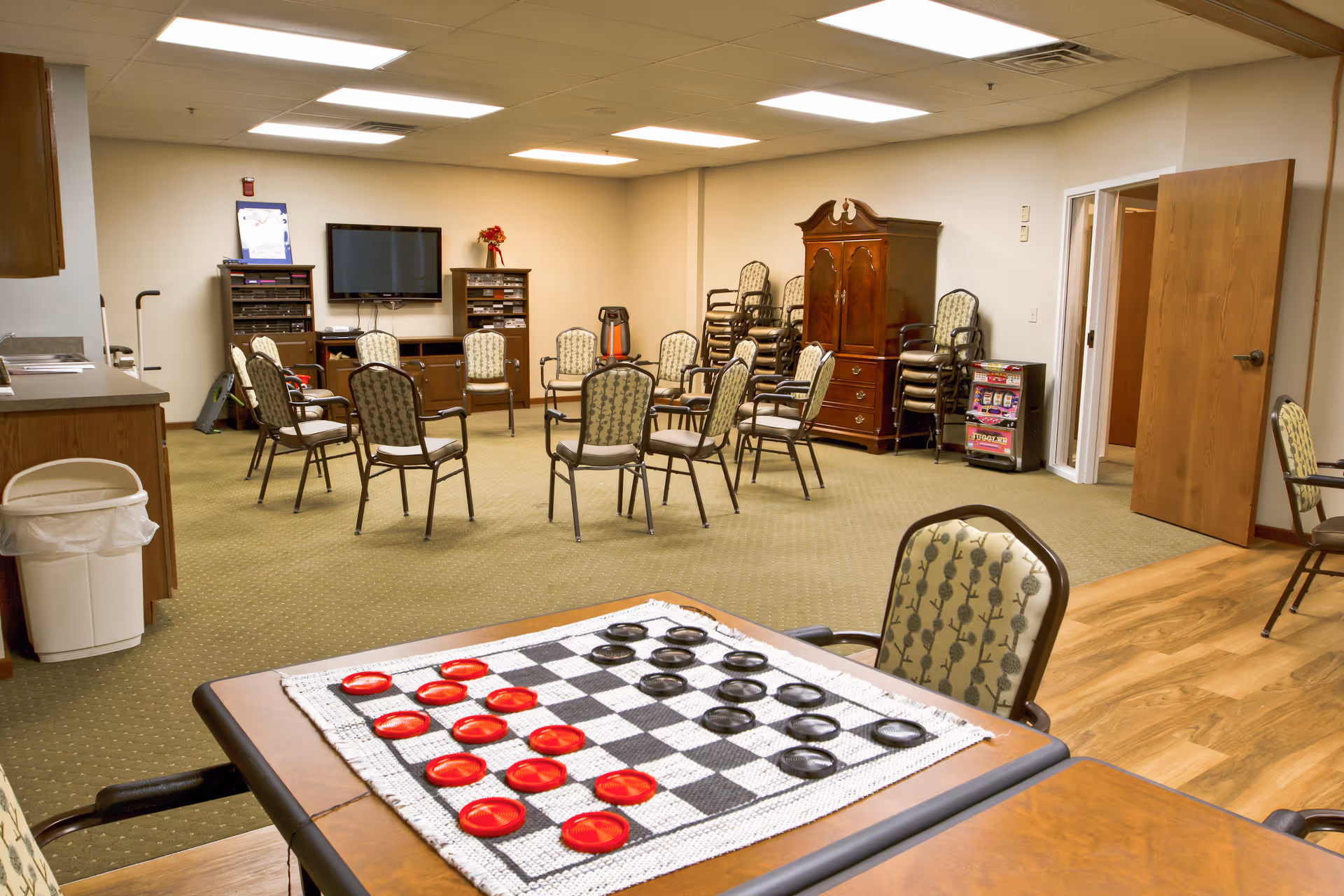 Activity room with arranged chairs, a checkers board on a table, and assorted furniture.