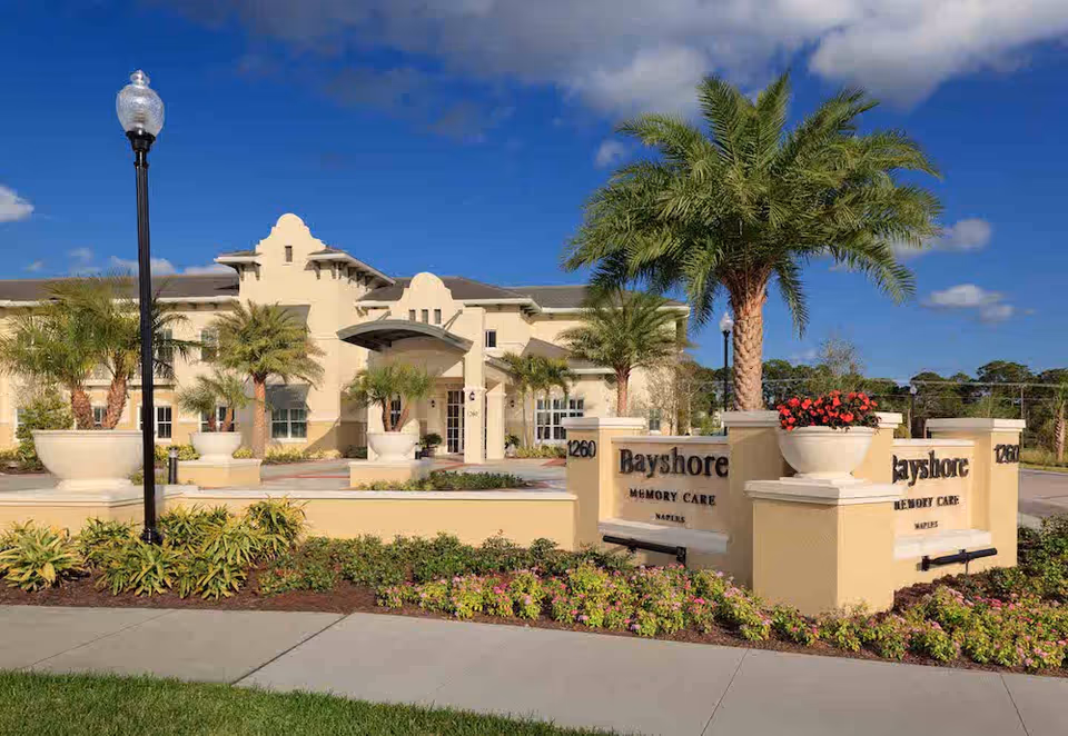 Sunny exterior view of Bayshore Memory Care entrance with palm trees and manicured landscaping.