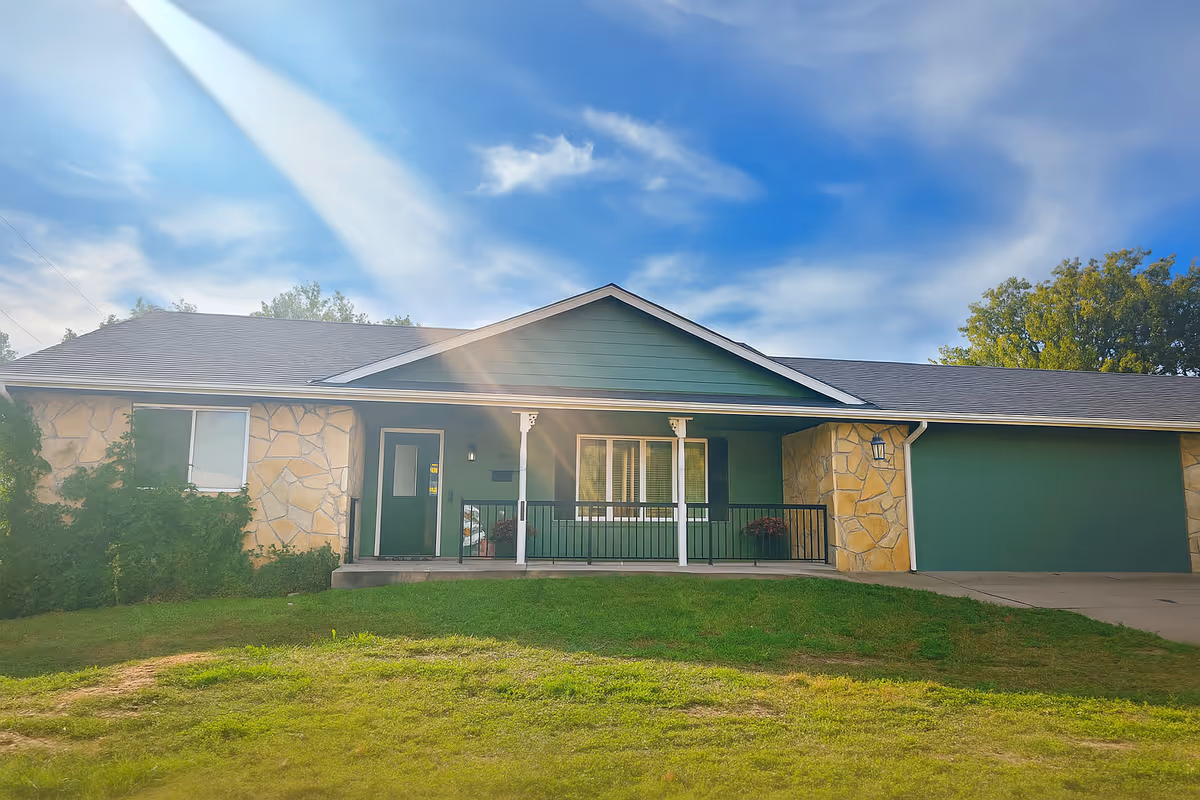 Single-story senior living facility with green doors, stone accents, and a front porch.