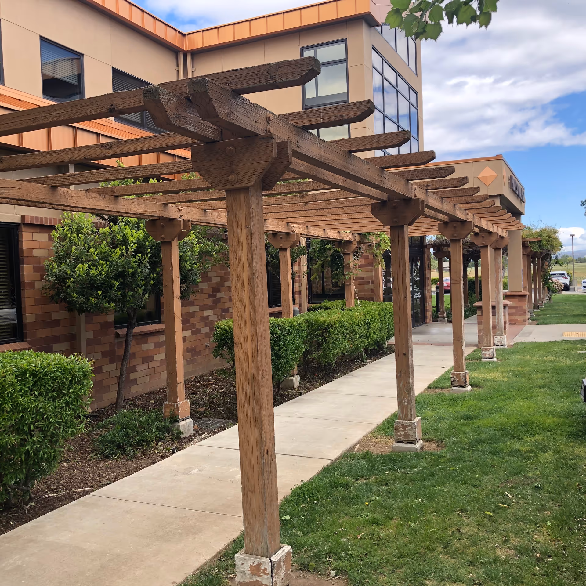 Wooden pergola walkway along the facility exterior with brick walls and greenery.