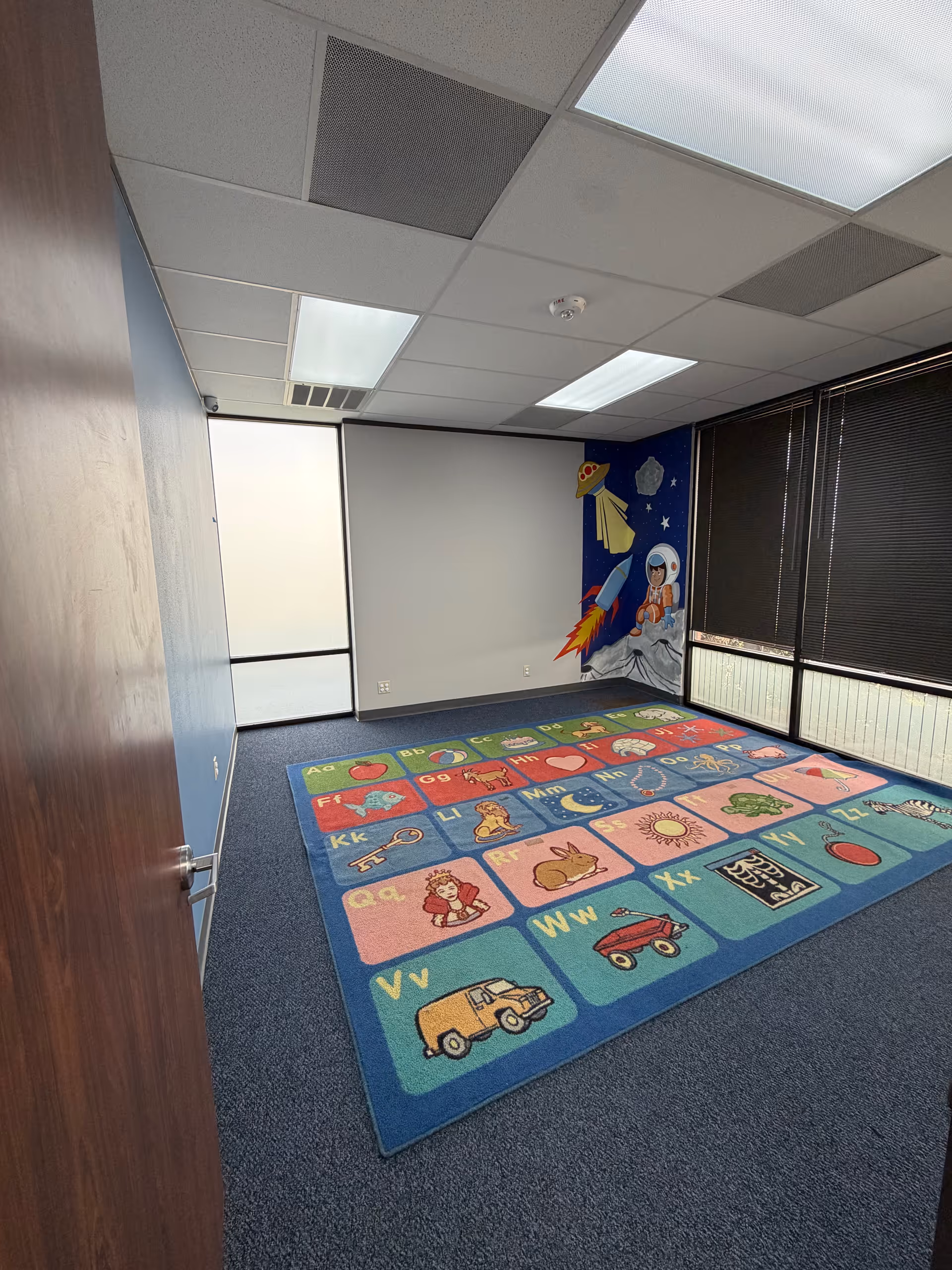 Colorful alphabet rug on the floor of a small interior activity room with a space mural.