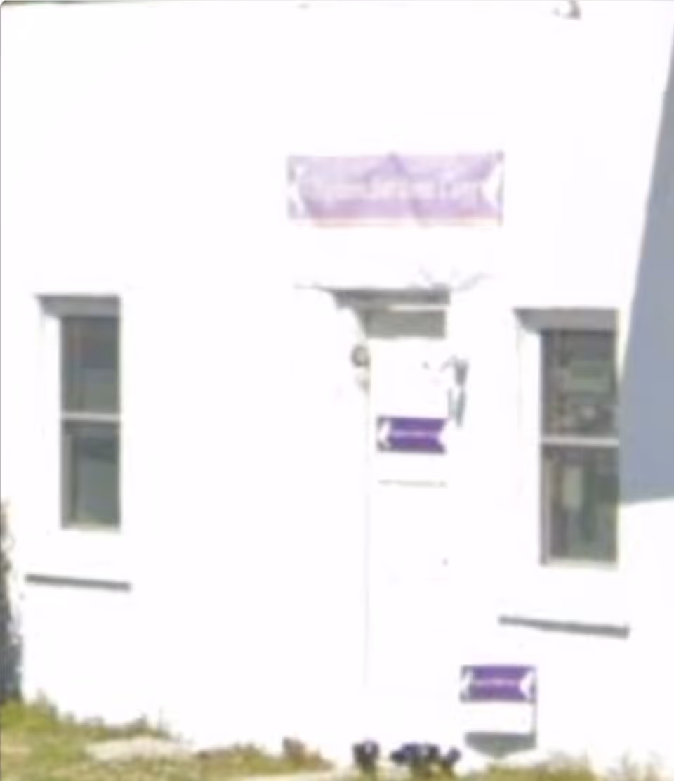 White building exterior with a purple sign, a small front door, and two windows