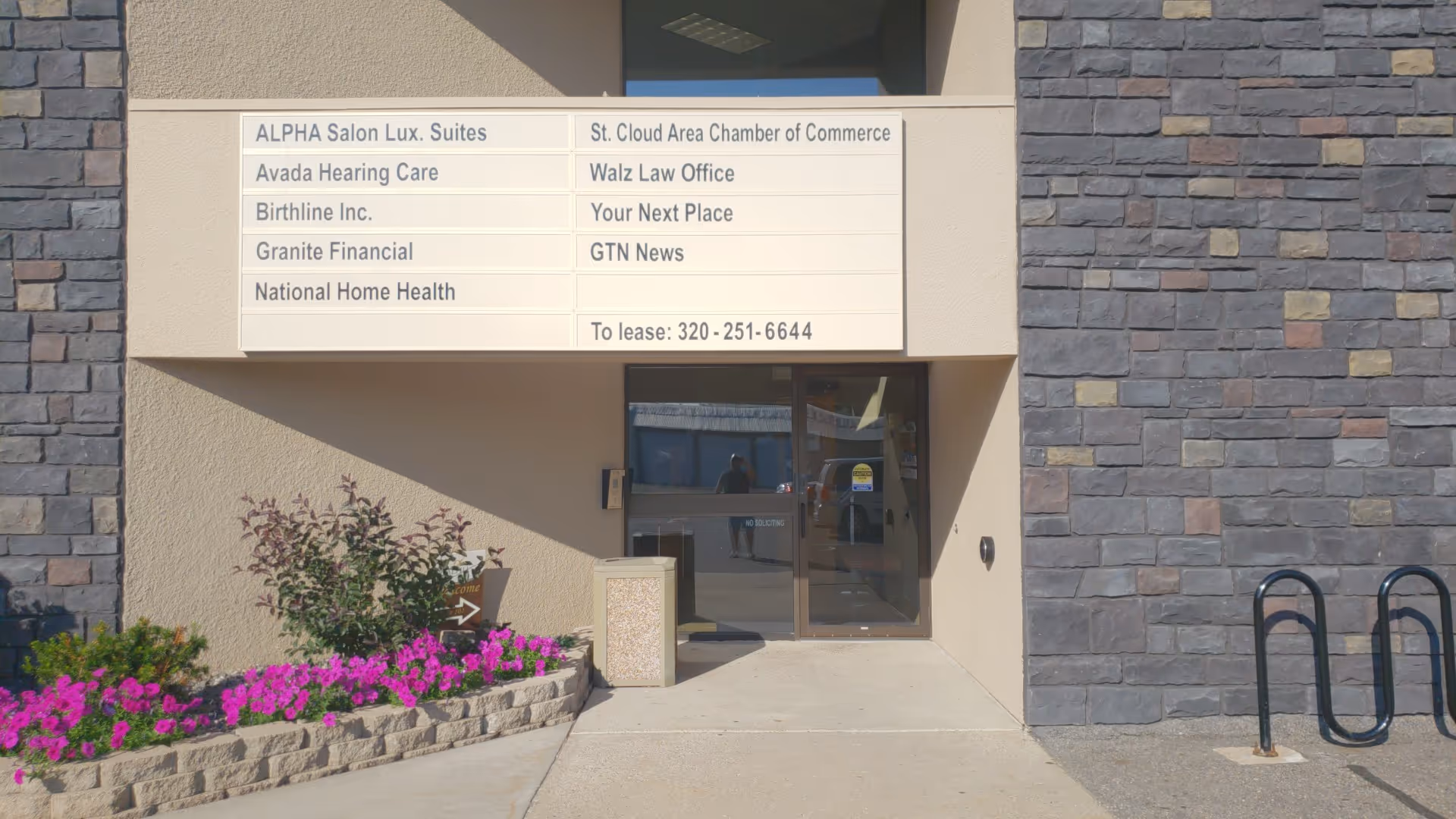 Exterior entrance of a beige building with a National Home Health directory sign and flowers.