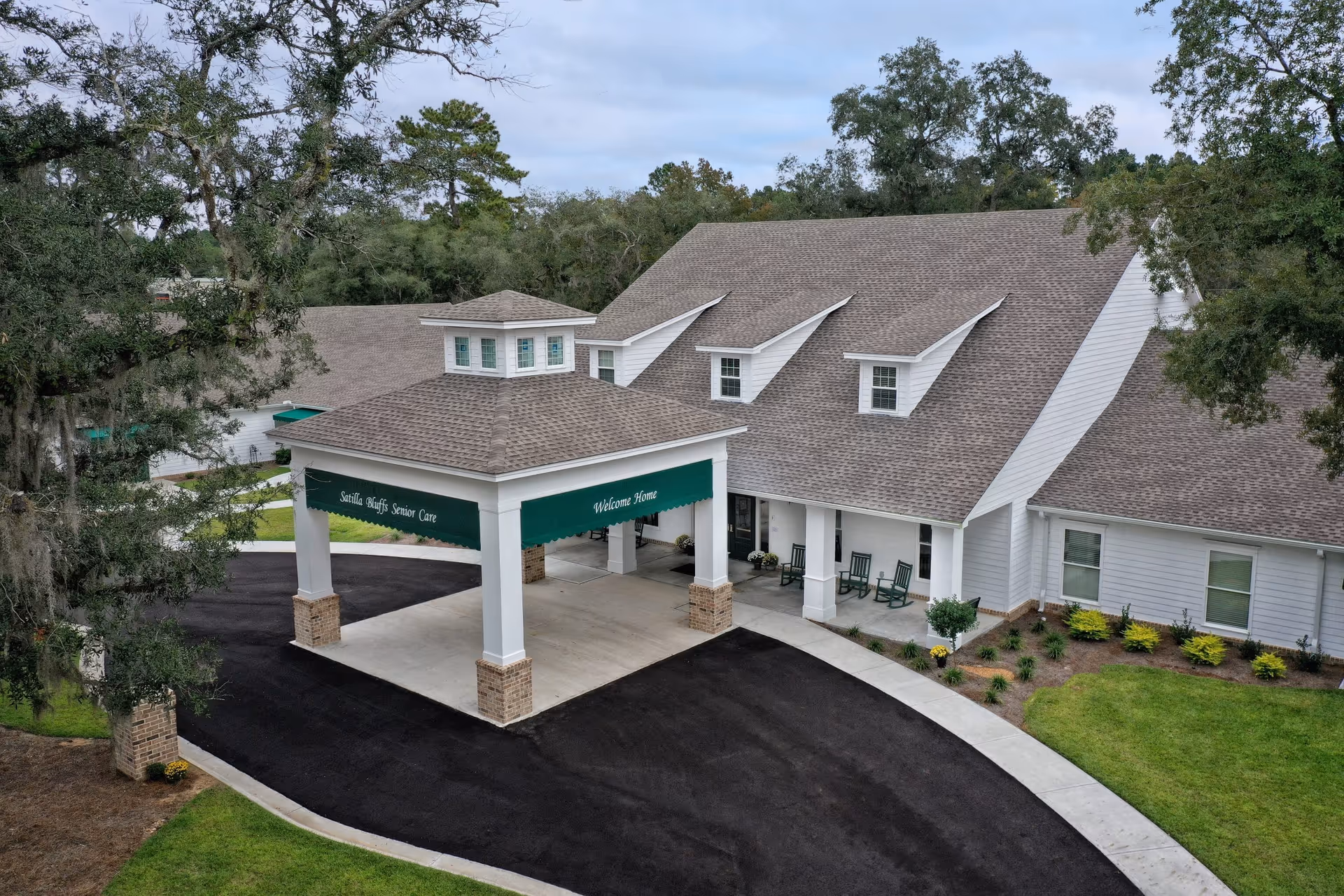 Front entrance of Satilla Bluffs Senior Care featuring a covered porte-cochere with green awnings and a porch with rocking chairs.