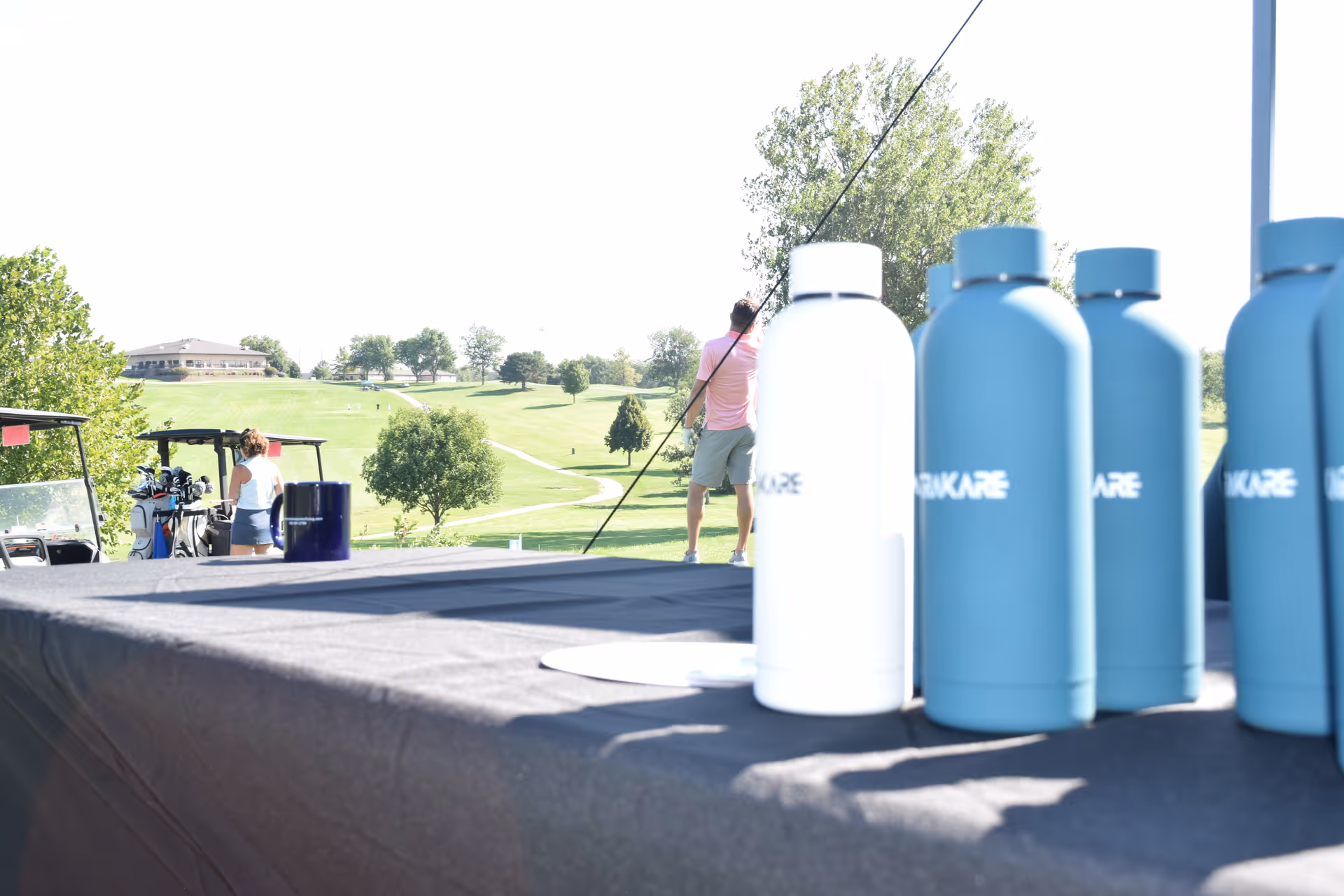 Outdoor event at a golf course with water bottles lined up on a table in foreground