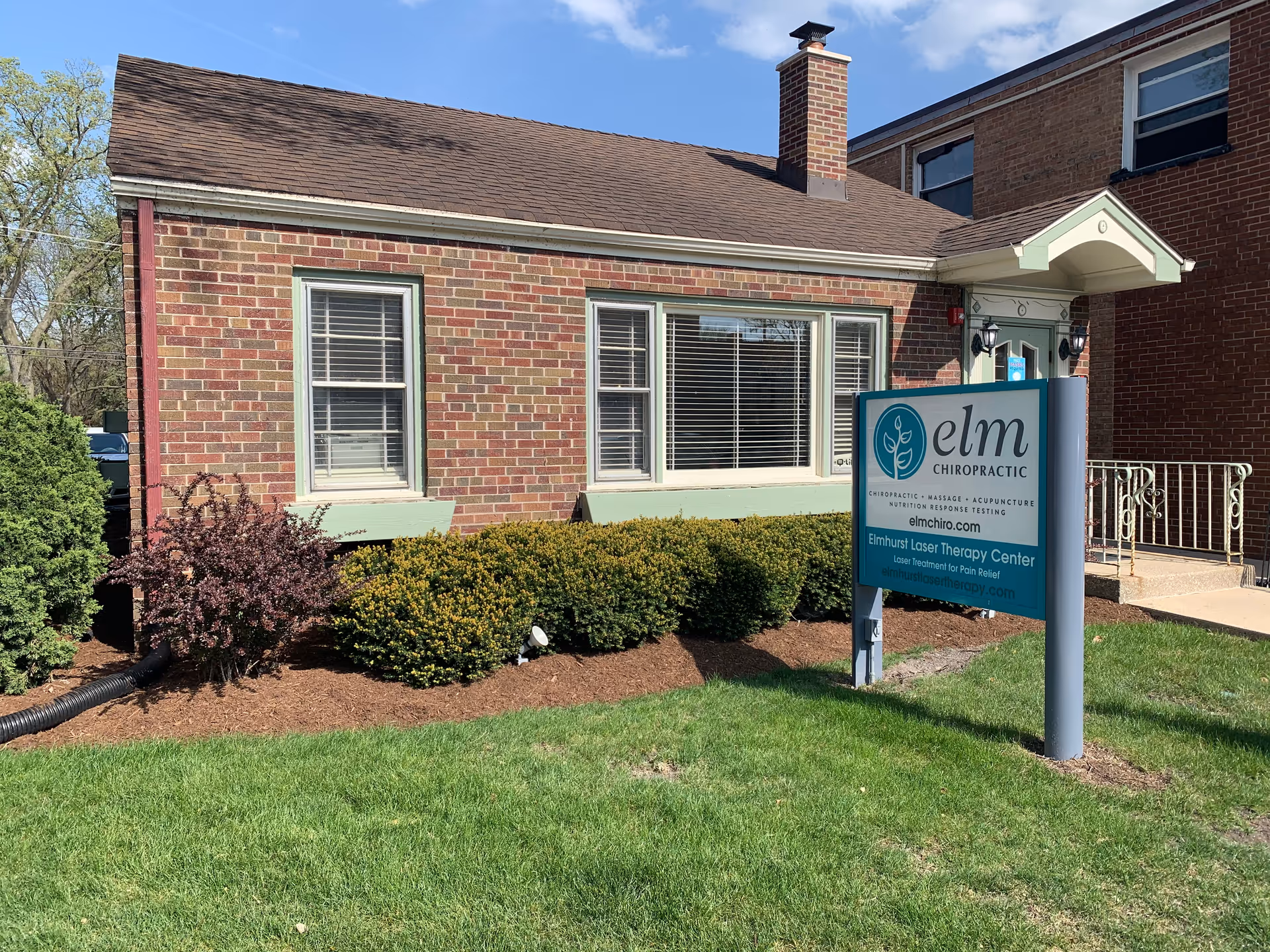 Brick building exterior with large windows and Elm Chiropractic sign in front yard.