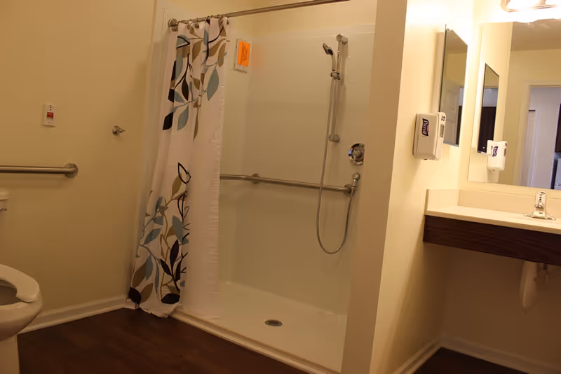 Accessible bathroom with a walk-in shower with grab bars and a floral shower curtain, sink, and toilet.
