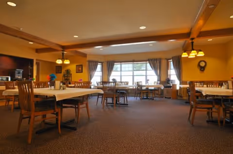 Windsor Manor dining room: warm, well-lit, with multiple tables, chairs, and large windows.