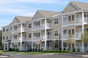 Multi-story beige senior living building with balconies and manicured lawn, sunny day.