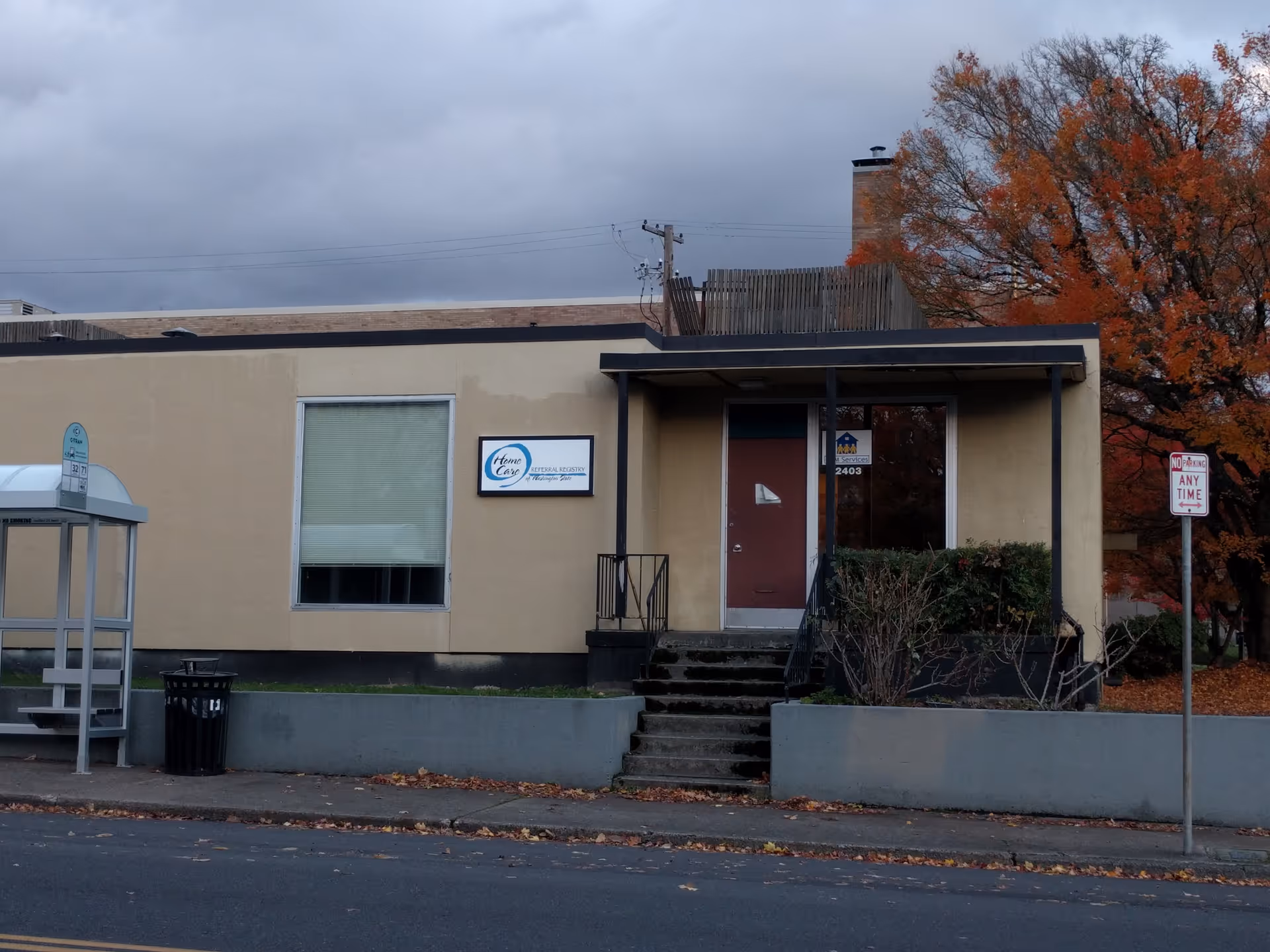 Beige single-story building with front entrance, signage, and autumn trees nearby.