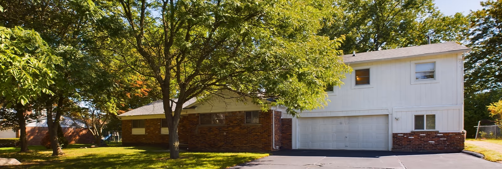 White two-story facility exterior with brick base, garage doors, and front-yard trees.