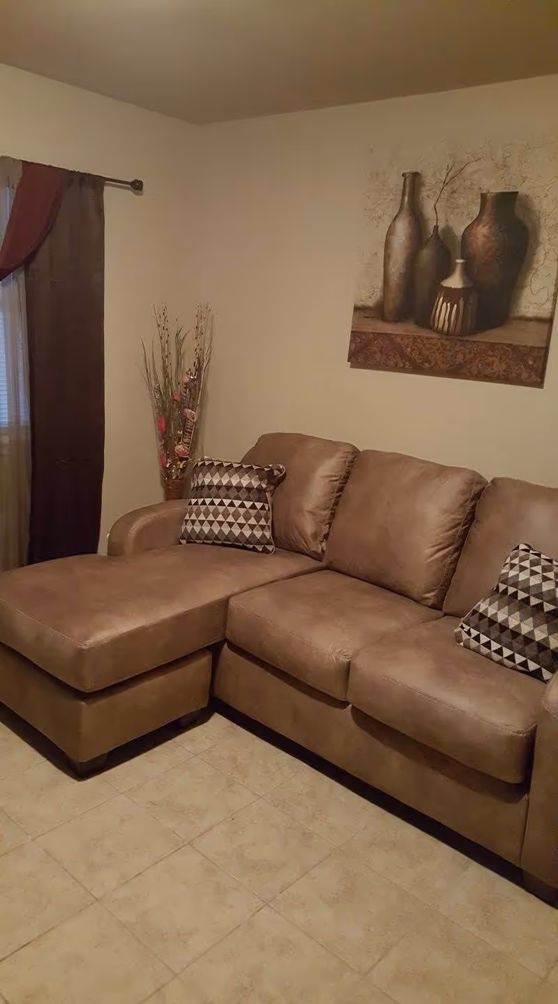 Brown sectional sofa in a cozy living room with wall art and curtains.
