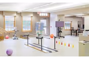 Therapy gym inside a senior facility with parallel bars and cones.