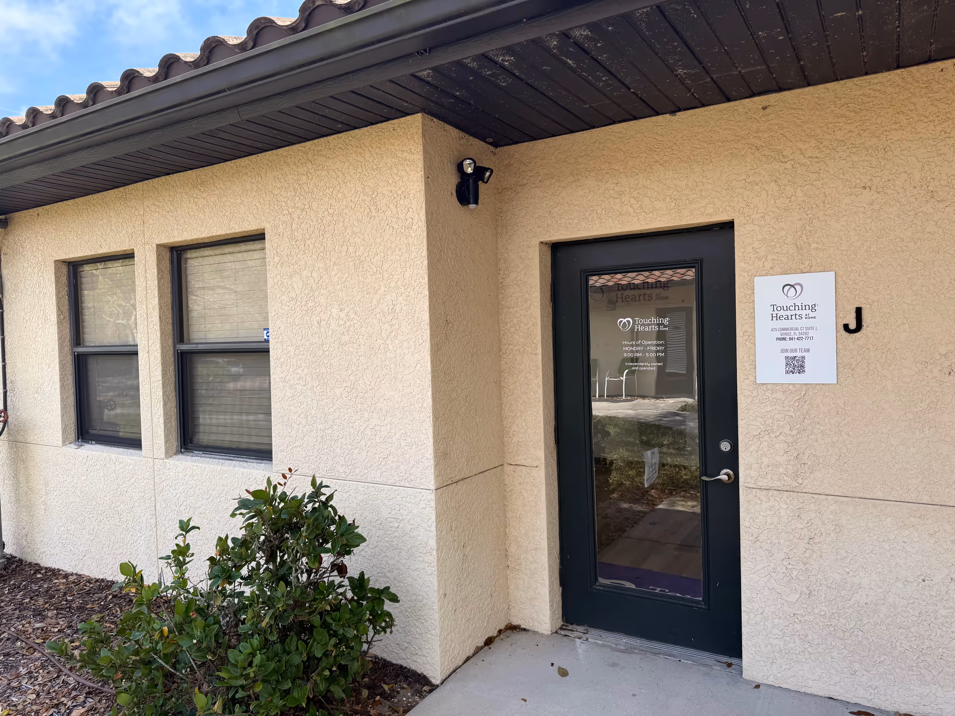 Exterior view of a building entrance with a glass door and Touching Hearts At Home sign.